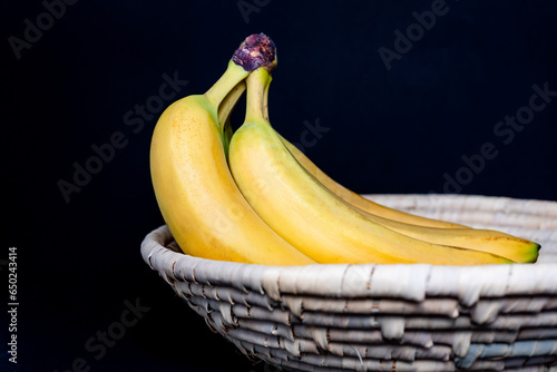 A bunch of Bananas in a wicker basket on a black background (ID: 650243414)