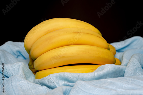 A bunch of bananas on a blue textile on black background (ID: 650243421)