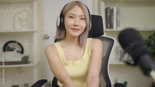 Cute young Asian woman audio DJ woman sing a song on microphone to broadcasting, Happy girl blogger music influencer recording wear headphone online live talk with listening audience in studio