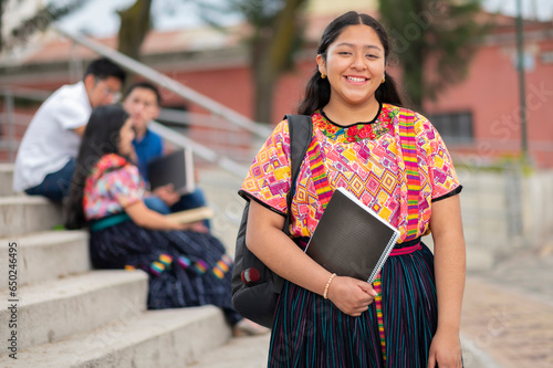 Beautiful Latina student of the Mayan ethnic group, with books in her hand, stands at the university and smiles at the camera. photo