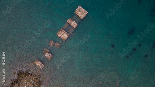 Aerial photo of a pier overlooking the sea, crystal clear water and stones.