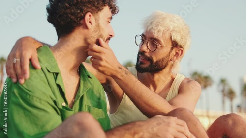 Young gay couple hugging while sitting on the beach