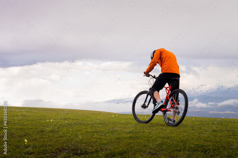Professional mountain biker on the background of mountains and green hills. Tired mtb rider in full face helmet outdoors