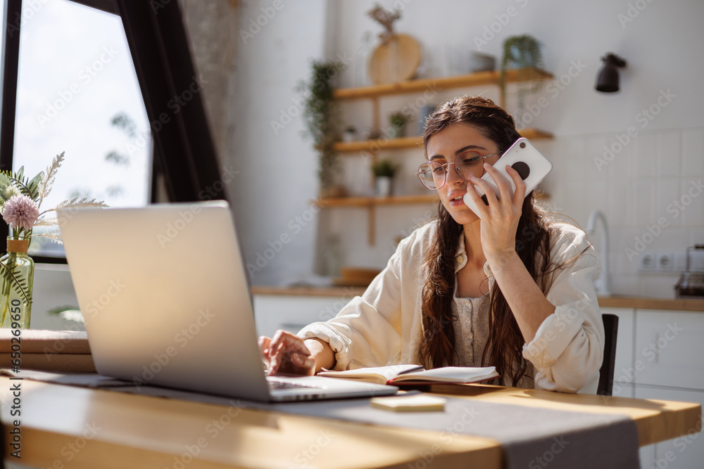 Woman recording voice message on smartphone and using laptop during online education at home Woman recording voice message on smartphone and using laptop during online education at home