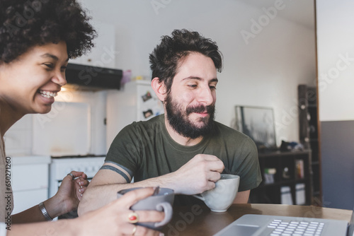 Young multiethnic couple using pc having coffee