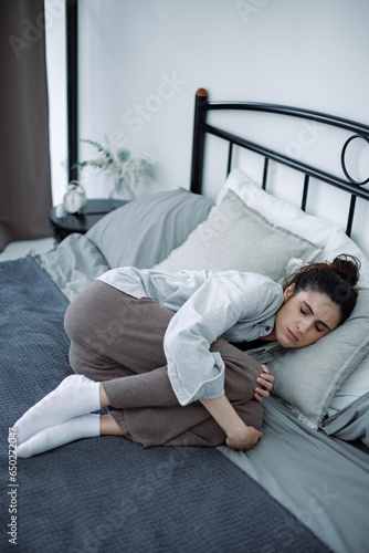 Lonely and sad brunette woman hugging knees while lying on bed at home, mental disorder concept