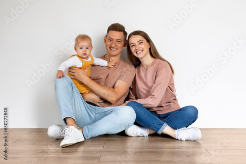 Portrait Of Parents With Cute Infant Child Sitting On Floor At Home