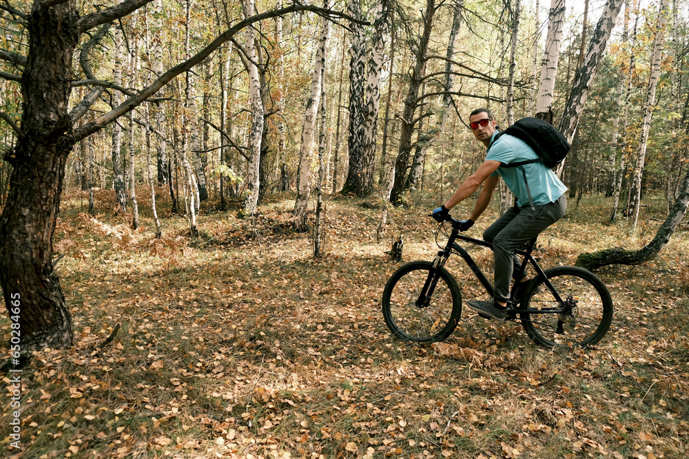 Travel by bike.A man with a backpack and gloves rides a mountain bike through the forest in autumn.An active lifestyle.Mountain Bike