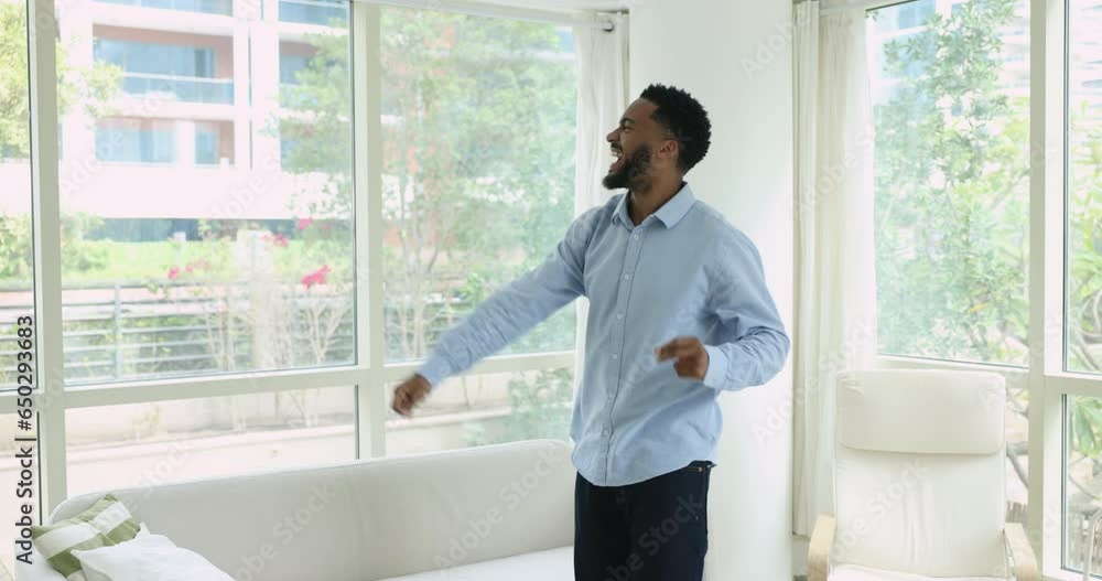 Hilarious young African man dancing alone in living room dancing, relish favourite track, singing cool popular song looks carefree having fun on weekend alone in modern living room. Hobby, enjoy life Hilarious young African man dancing alone in living room dancing, relish favourite track, singing cool popular song looks carefree having fun on weekend alone in modern living room. Hobby, enjoy life