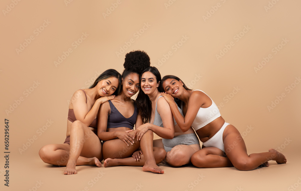 Group of young international women in different underwear with natural beauty, sitting on floor on beige background