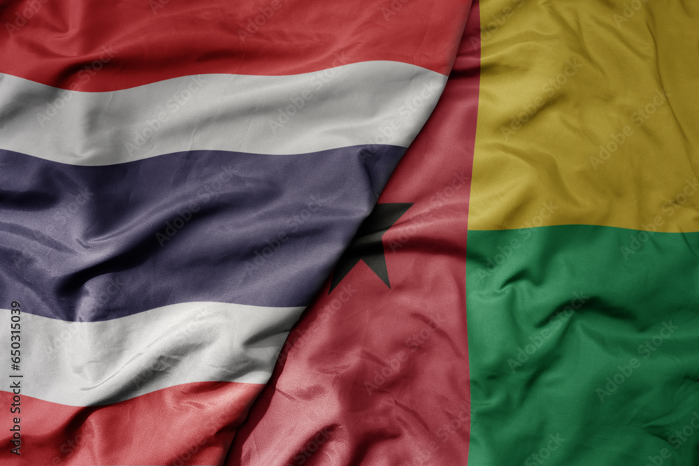 big waving national colorful flag of thailand and national flag of guinea bissau .