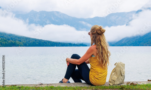 Thoughtful Woman sitting and looking at lake with alps mountain with mist