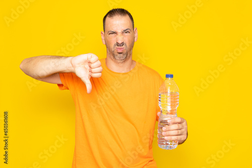 Hispanic man with beard in his 40s making the gesture of I don't like having to buy plastic bottles for water, isolated over yellow background