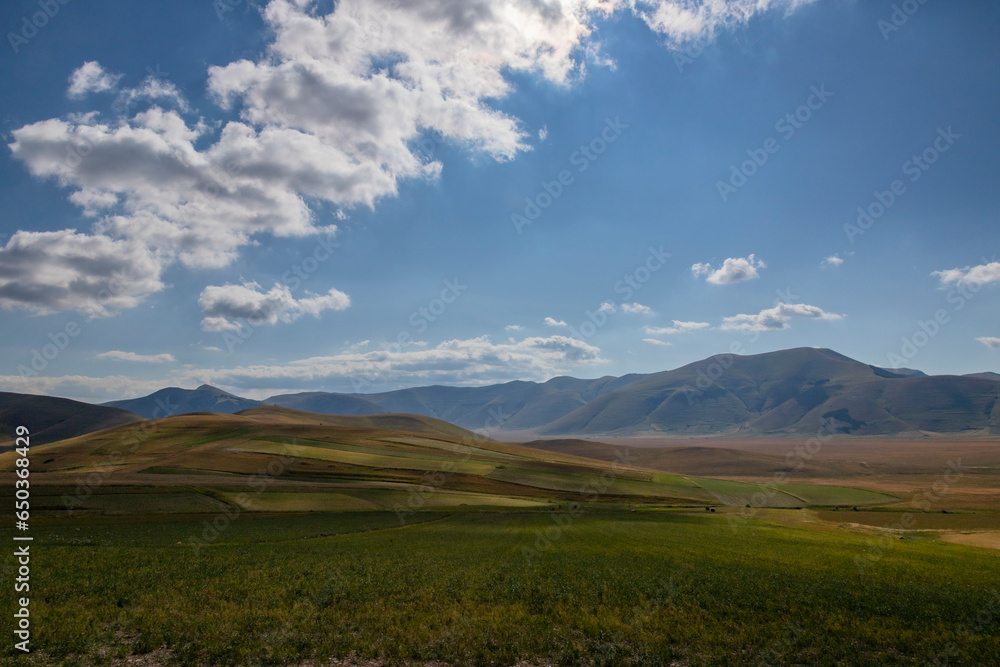 Famous mountain village of Castelluccio di Norcia with beautiful summer landscape at Piano Grande (Great Plain) mountain plateau in the Apennine Mountains on a cloudy day, Umbria, Italy. Low key.