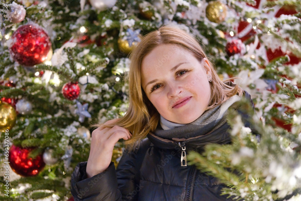 Portrait of beautiful smiling European woman on Christmas tree background. Young happy woman in new year holidays.