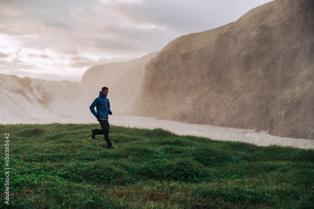 A sportsman is running in nature next to the waterfall in Iceland. A sportsman is running in nature next to the waterfall in Iceland.