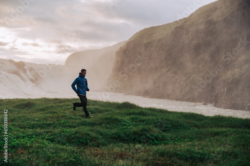 A sportsman is running in nature next to the waterfall in Iceland.