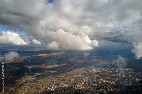 Aerial view from airplane window at high altitude of distant city covered with puffy cumulus clouds forming before rainstorm