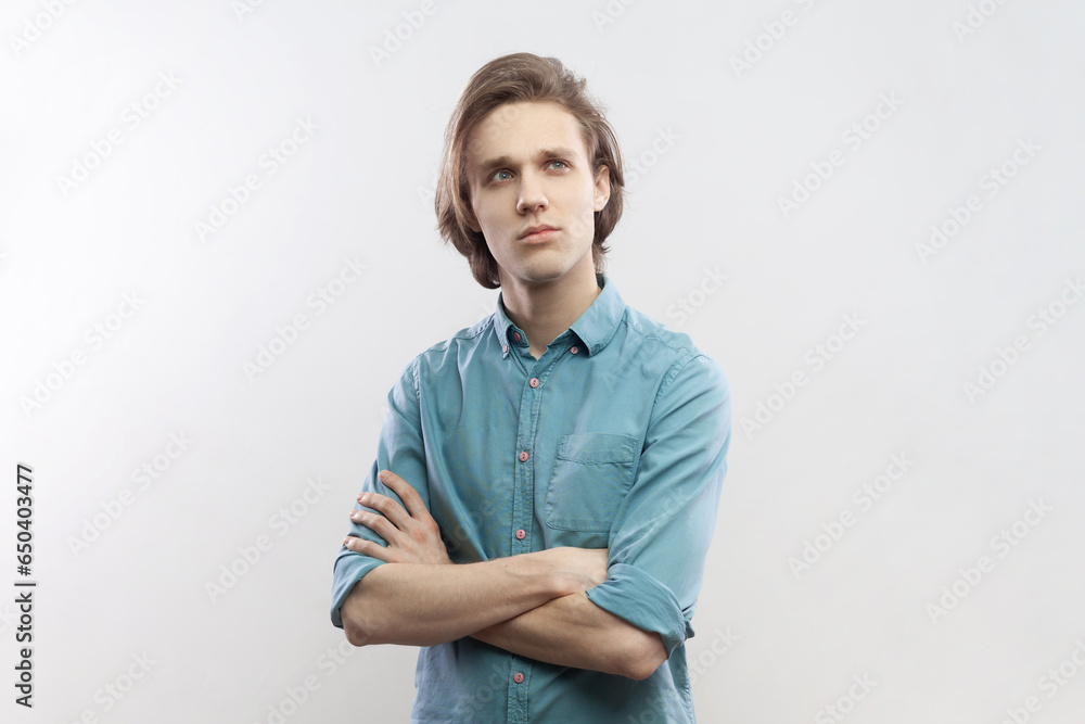 Portrait of pensive thoughtful handsome young man standing with folded hands, thinking, planning, pondering, wearing blue shirt. Indoor studio shot isolated on gray background. Portrait of pensive thoughtful handsome young man standing with folded hands, thinking, planning, pondering, wearing blue shirt. Indoor studio shot isolated on gray background.