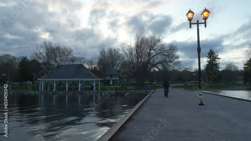 Adult man riding a bicycle on the lake pier at dusk in Couchiching Beach Park, Orillia, Canada photo