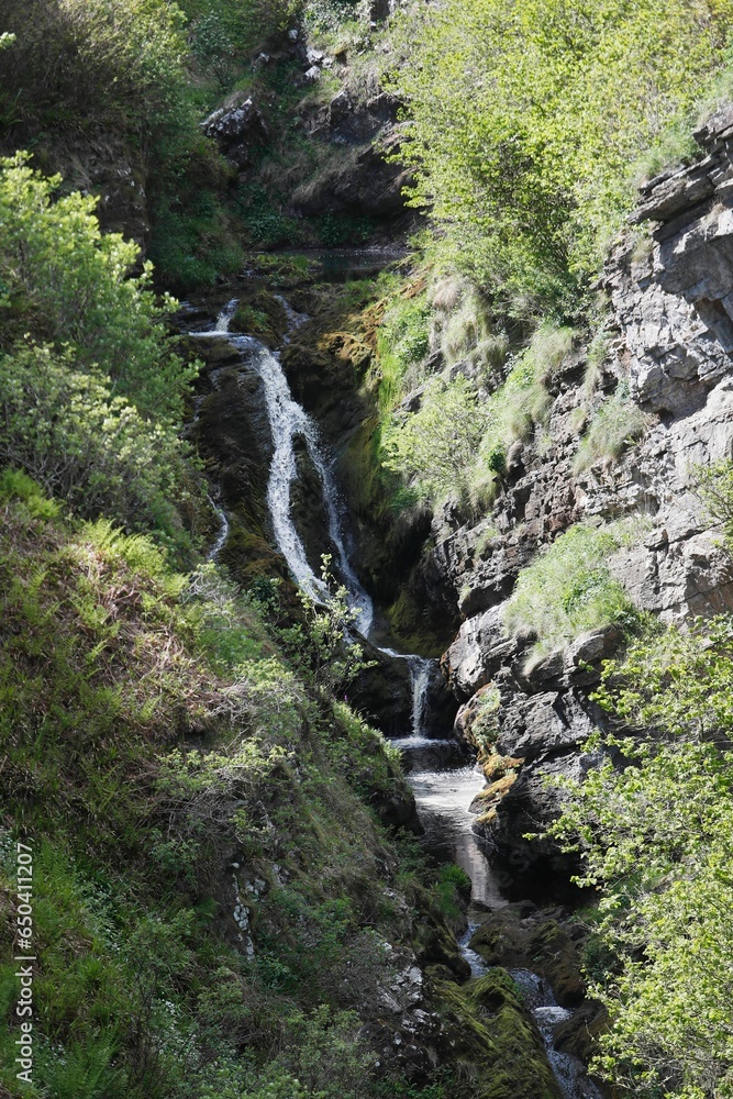 Majestic waterfall cascades down a rocky cliffside, into a lush green valley below in Lybster