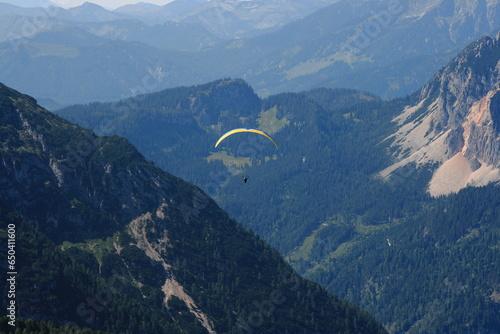 Alps. Dachstein Mountains. Austria. Paraplaner gliding in blue sky with view on Alpine mountains on paraplane