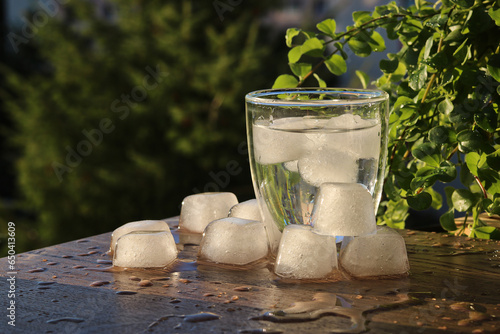 A glass of water with ice and ice cubes on a table top in the garden
