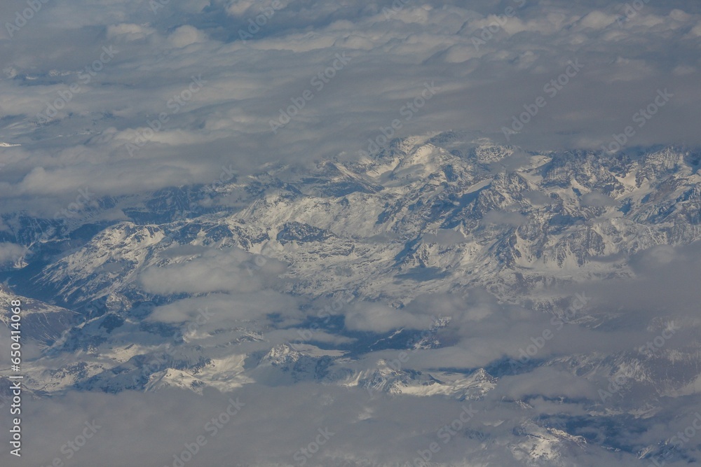 Aerial view of a mountain range covered with snow in clouds