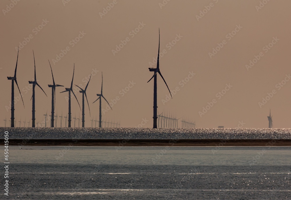Φωτογραφία Cluster of wind turbines on a beach, illuminated by the golden light of a settin