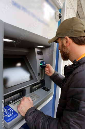 Vertical shot of a bearded male customer using debit, and credit card to complete a transaction via ATM automated teller machine