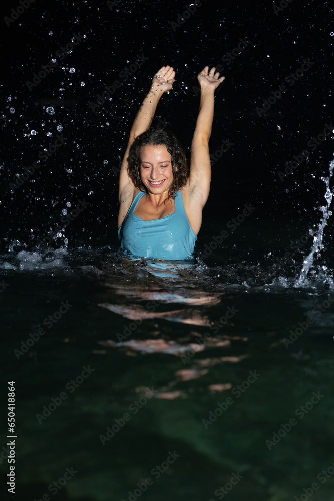 A beautiful and curly young woman in a blue swimsuit is frolicking in the sea at night A beautiful and curly young woman in a blue swimsuit is frolicking in the sea at night