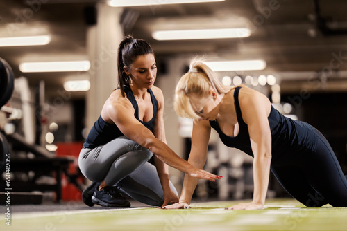 A female personal trainer is training sportswoman who is doing pushups in a gym.