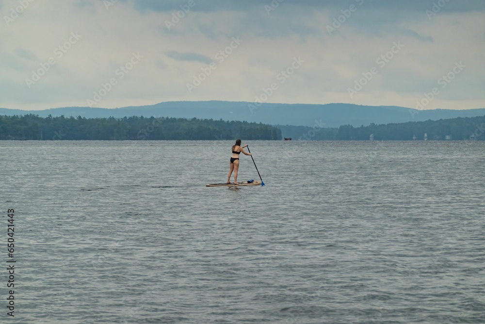 Naklejka premium Paddle boarder enjoying a view of the White Mountains cruising on New Hampshire's Lake Winnipesaukee