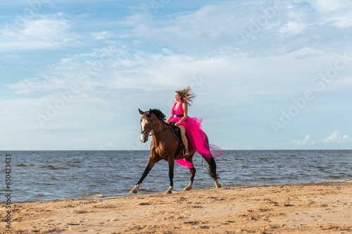 Woman wearing a pink dress on a galloping horse on a sunny beach