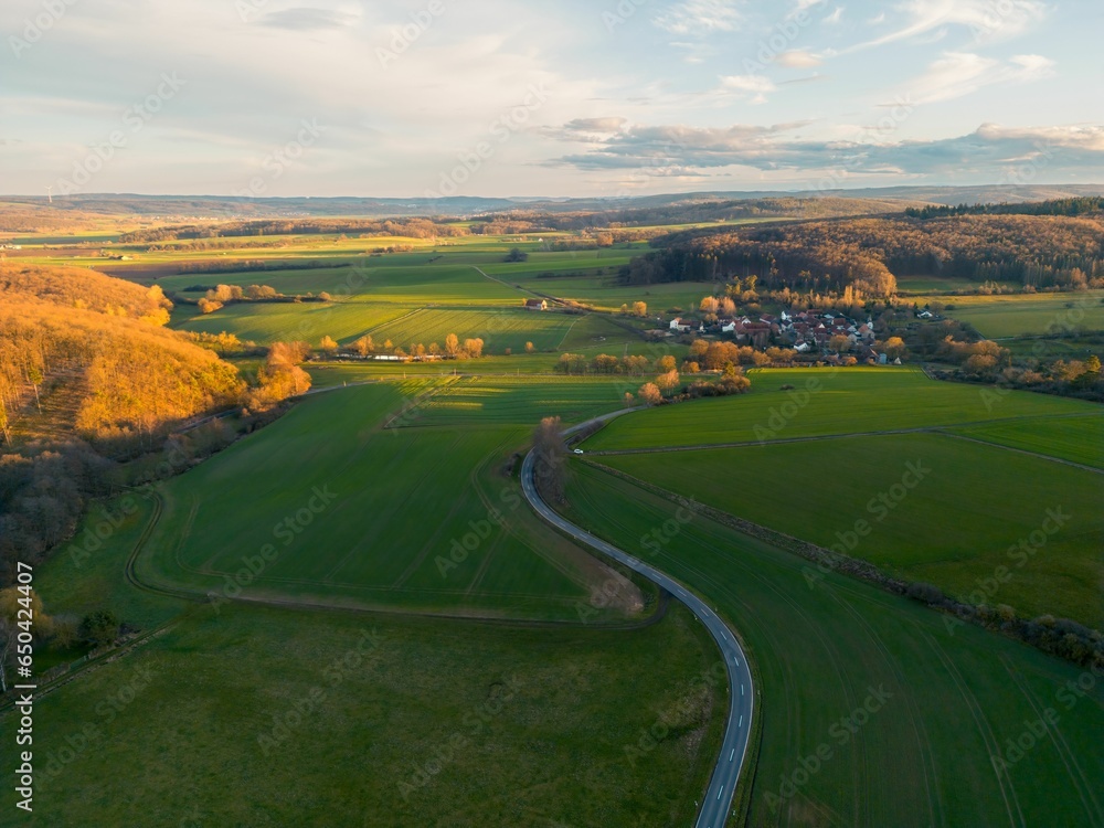 Drone view of a road surrounded by greenery in the countryside during the golden hour