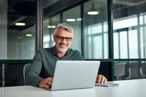 Content Older Business Professional, Grinning as He Tackles Tasks on His Laptop, Working Comfortably from His Desk