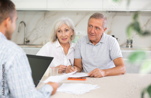 Salesman seller shows on laptop details of purchase to elderly couple. Health insurance concept photo