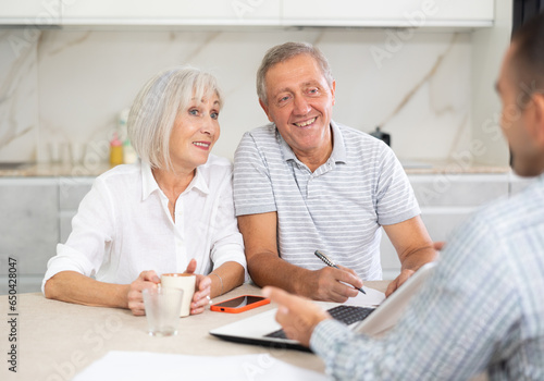 Elderly couple listens attentively to insurance manager while at home. Health insurance concept