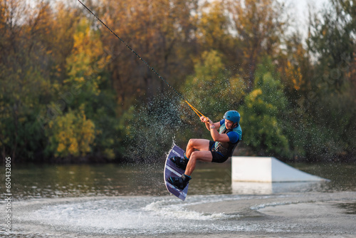 An athlete jumps over the water. Wakeboard park at sunset. Rider performs a trick on the board