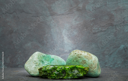 green chrome diopside stone on a dark gray background for a product presentation podium. natural green stones on a gray background for the presentation of perfumes, jewelry, cosmetics, medicines. photo