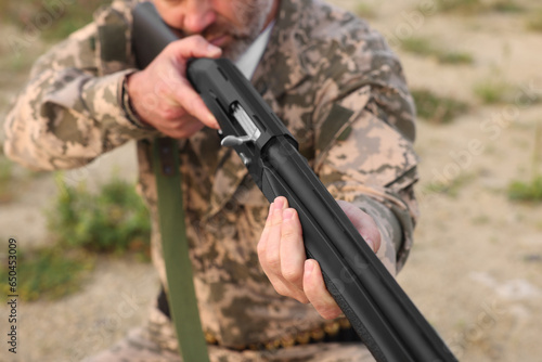 Man wearing camouflage and aiming with hunting rifle outdoors, closeup