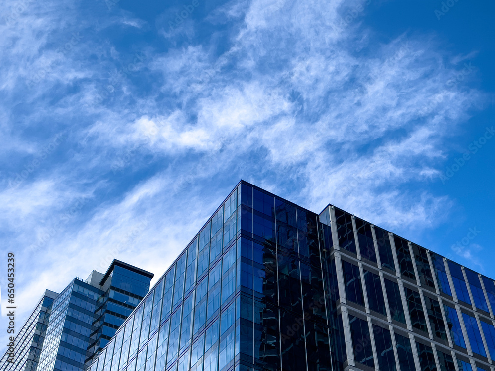 Angled view of a large, window covered building corner against a blue, cloud filled sky Angled view of a large, window covered building corner against a blue, cloud filled sky