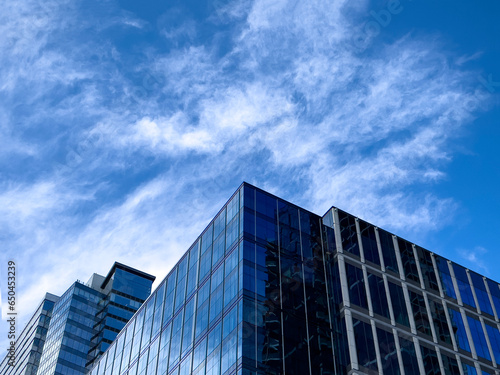 Angled view of a large, window covered building corner against a blue, cloud filled sky