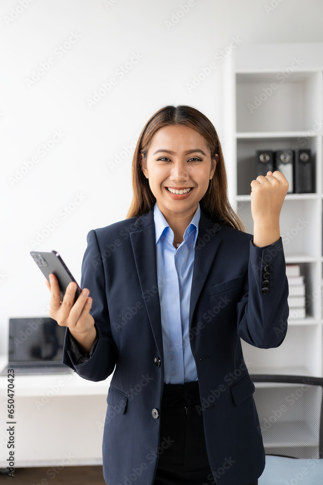 Young Asian business woman wearing suit and using laptop on gray baclground Cheerful young woman celebrating her achievement while reading good news on laptop from home office Young Asian business woman wearing suit and using laptop on gray baclground Cheerful young woman celebrating her achievement while reading good news on laptop from home office