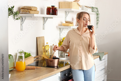 Young woman drinking wine while boiling spaghetti in kitchen