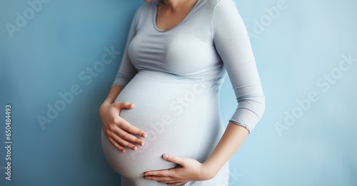 Unrecognizable pregnant woman smiling and holding her big belly caringly against blue wall background. Generative AI