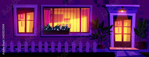 House facade at night with light from windows and lamp above entrance. Cartoon brick wall of building with windows and doors, wooden fence and plants in pots. Dark evening exterior of rural home.