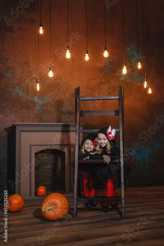 Little witches stand leaning on the stairs, smiling.