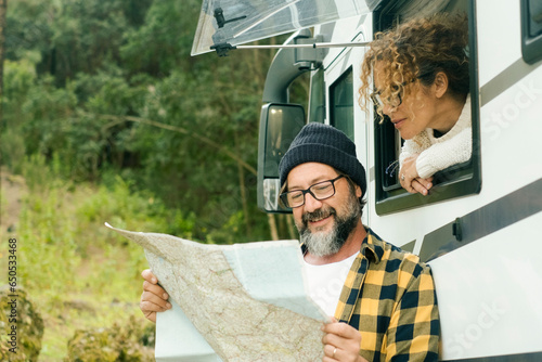 One happy traveler couple looking together a paper guide map to choose plan next travel destination. Living in a van. Nomadic people, Vanlife. Alternative vehicle vacation journey. Road trip planning