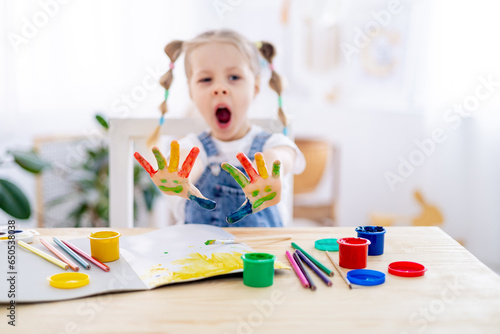 hands in focus, portrait of a yawning little child girl with stained multicolored hands in finger gouache or in paint, boring drawing lessons